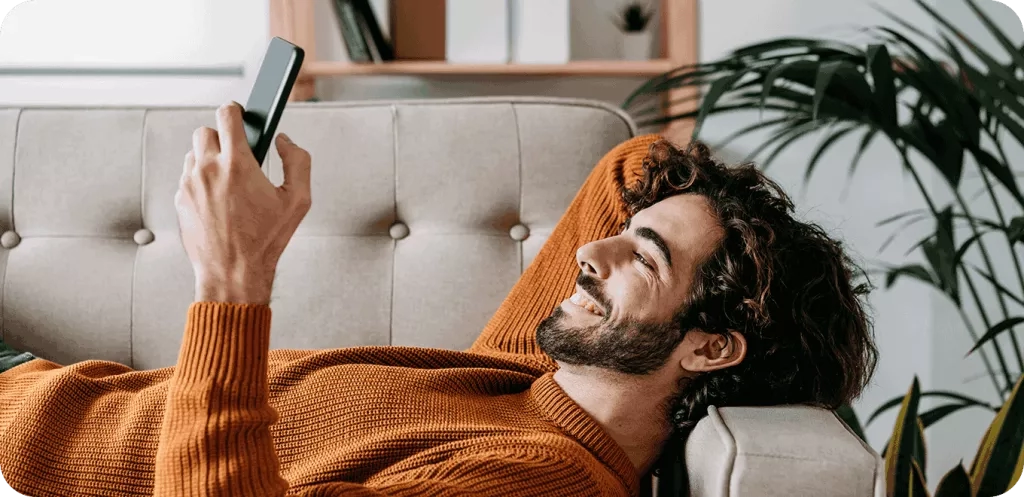 A person lying down on a sofa looking at a mobile phone.